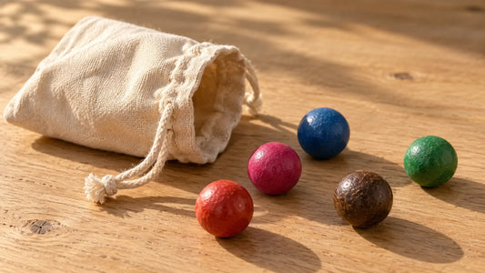 Petit sac de toile écrue ouvert sur une table de bois, cinq billes en terre MesBilles de couleurs différentes posées à côté